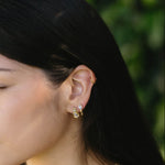 Close-up of a woman wearing gold earrings and necklaces with a blurred green background