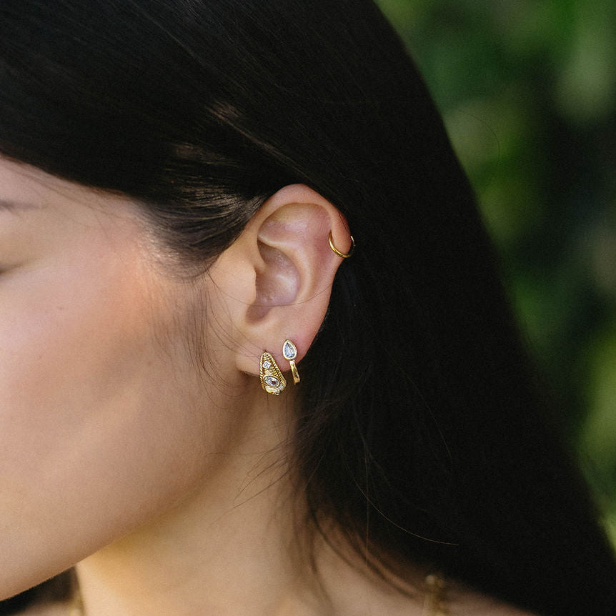 Close-up of a woman wearing gold earrings and necklaces with a blurred green background