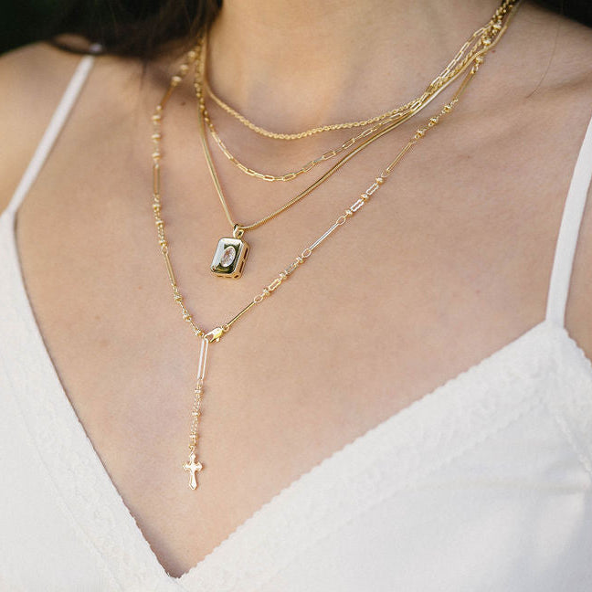 Close-up of a person wearing multiple gold necklaces with a blurred green background