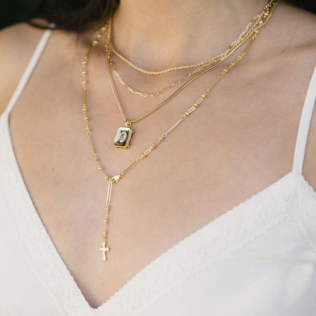 Close-up of a person wearing multiple gold necklaces with a blurred green background