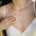 Woman wearing a gold necklace with pearl accents and rings on a blurred natural background