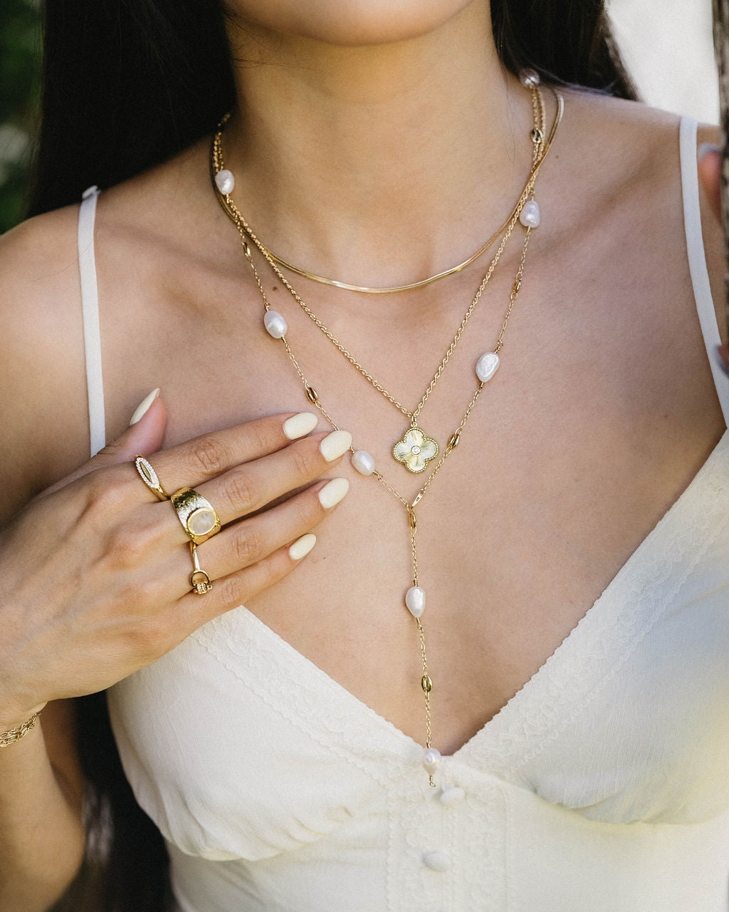 Woman wearing a gold necklace with pearl accents and rings on a blurred natural background
