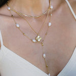 Close-up of a woman wearing a gold necklace with floral design and pearl accents.