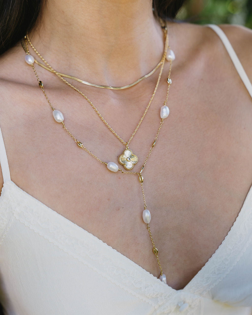 Close-up of a woman wearing a gold necklace with floral design and pearl accents.